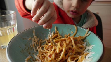 Çocuk çatalı kapar ve akşam yemeğinde bir lokma makarna yer. Makro yakın plan yüz, İtalyan yemeği.