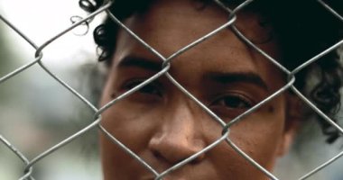 Genç siyahi bir kadın çitin arkasında kapana kısılmış, eli kapalı ve yalnızlık içinde gözleri kapanan bir kadın. Metal bariyer arkasında depresyon tasvir eden 20 'li yaşlarda zihinsel hastalıklarla boğuşan biri.