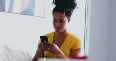 Genç Afrikalı Amerikalı kadın evdeki kanepeye mesaj atıyor. 20 'li yaşlarda Latin kökenli samimi bir kız arkadaşlarıyla internet üzerinden iletişim kurmak için modern teknolojiyi kullanıyor.