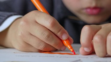 Yoğunlaşmış çocuk masada turuncu fosforlu kalemle çizer