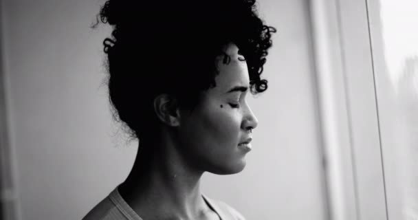 劇的なモノクロマティック 黒と白の瞑想的な感情と距離を眺めながら窓から立っている一人の熟考の若い黒人女性 プロフィールのクローズアップフェイス — ストック動画