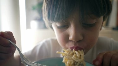 Makarna yiyen çocuk, aç 5 yaşındaki küçük çocuk karbonhidrat yiyor, peynirli spagetti yiyor, yakın plan yüz ve yemek yiyor.