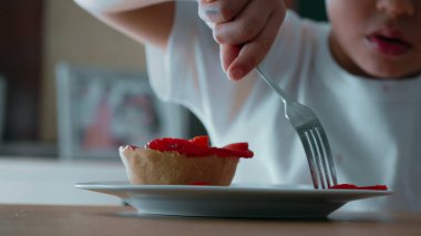Child Struggling to Reach Cheesecake with Fork - Close-Up View of Sugary Treat Topped with Strawberries on Plate clipart