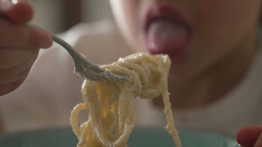 Çocuk elinde çatalla spagetti çeviriyor. Küçük çocuk makarna yemeyi öğreniyor, karbonhidrat zengini.
