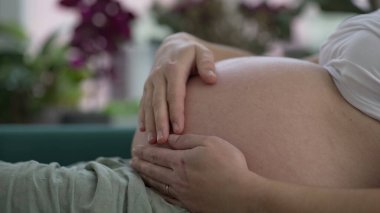 Hamile bir kadın yeni bir hayat umuduyla karnını okşuyor.