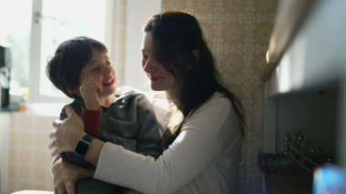 Ev mutfağında anne-çocuk kaynaşması. Otantik sevgi dolu bir an. Oğlu ve ebeveyni arasında. Küçük çocuk annesini yanağından öpüyor.