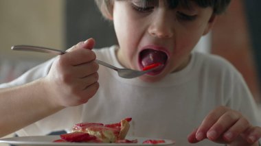 Little boy eating pieces of strawberry with fork, child enjoys sweet dessert after mealtime, kid meticulously selecting slices of fruit from cheesecake clipart