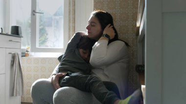 Anne, mutfak duvarına yaslanıp 5 yaşındaki oğlunu tutarken elleriyle burnuna dokunuyor. Kadın burnunu tırmalıyor, yüzüne dokunuyor.