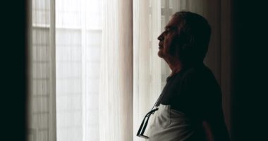 Depresyonda olan yaşlı bir adam, gölgelerin içinde dikilip, iç mekandan içeriye bakan, iç mekandaki üzgün, beyaz saçlı, 70 'li yaşlarda beyaz bir adam.