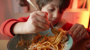 Spagetti yiyen küçük bir çocuğun portresi, 5 yaşındaki çocuğun neşeli yemek saati, makarnalı çatal çevirmede ustalaşması.