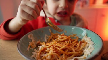 Spagetti yiyen küçük bir çocuğun portresi, 5 yaşındaki çocuğun neşeli yemek saati, makarnalı çatal çevirmede ustalaşması.