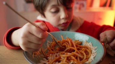 Spagetti yiyen küçük bir çocuğun portresi, 5 yaşındaki çocuğun neşeli yemek saati, makarnalı çatal çevirmede ustalaşması.