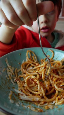 Küçük çocuk elinde çatalla spagetti çeviriyor. Çocuk akşam yemeğinde makarna yiyor, İtalyan yemeği yiyor. Dikey video