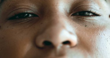 Meditasyon yapan genç siyah bir kadın rahatlama ve tefekkür için gözlerini kapatıyor. Makro yakın plan yüz hatları sessizce dinlenirken, kameraya gülümseyerek gözlerini açar.