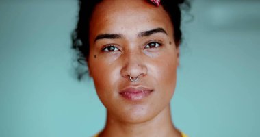 Bir genç siyah Latin kadın kameraya tarafsız bir ifadeyle bakıyor. 20 'li yaşlarda, Afrika kökenli, yakın plan yüzlü bir Güney Amerikalı kadın.