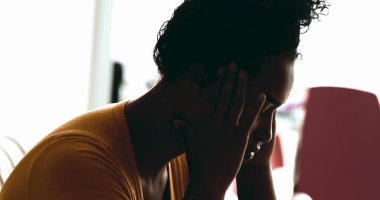 Genç Afrikalı Amerikalı kadın evde depresyonla boğuşuyor. Stres ve keder altında eziliyor. Baş ağrısı çeken elleri şakaklara koyuyor.