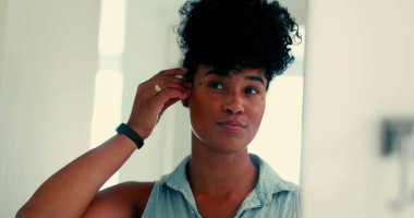 Genç, mutlu, siyah Brezilyalı bir kadın aynanın önünde saç stilini değiştirip dışarı çıkmaya hazırlanıyor. Zarif Afrikalı Amerikalı 20 'li yaşlarda gülümseyen kendine güvenen yetişkin bir kız.