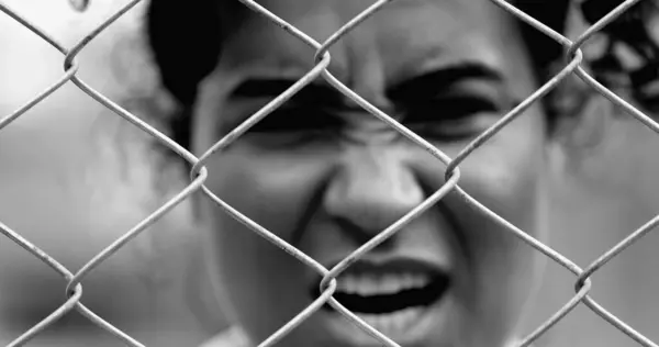 stock image Desperate Young African American woman feeling outrage screaming with rage behind metal fence barrier frowning and open mouth screaming in anger
