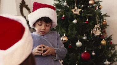 Kırmızı Noel şapkası takan yakışıklı çocuk ve pijamalı açılış hediyesi. Sabah aile üyeleri etrafını sarmış.