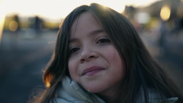 小さな女の子の肖像画は 日没時のバックライトの間に笑顔のカメラに向かって頭を向ける 8歳の子供のクローズアップフェイスが幸せを感じる — ストック動画