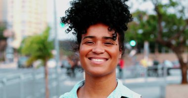 Afrika kökenli mutlu, kıvırcık saçlı, şehir ortamında gülümseyen siyah bir kadın. Güney Amerikalı yetişkin bir kızın portresi.