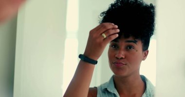 Genç siyah bir kadın aynanın önünde kıvırcık saçlarıyla dışarı çıkmaya hazırlanıyor. 20 'li yaşlarda, Afrika kökenli Latin bir kadın saç stili ayarlıyor.