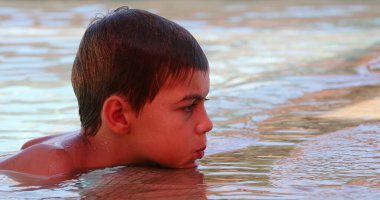 Yüzme havuzunda tek başına oynayan samimi, düşünceli bir çocuk havuz kenarında çenesini tutmayı düşünüyor.