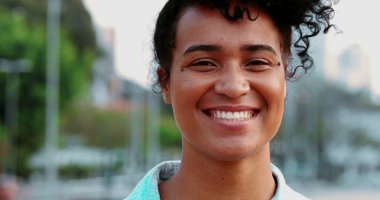 Genç, mutlu bir Brezilyalı kadın, gülerek ve gülerek kentin dışında duruyor. Neşeli kişinin portresi otantik dostça ifade