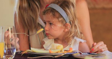 Anne kucağında oturan çocuk birlikte öğle yemeği yiyor.