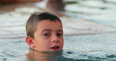 Havuzdaki küçük çocuk kamerayla oynuyor ve gülümsüyor.