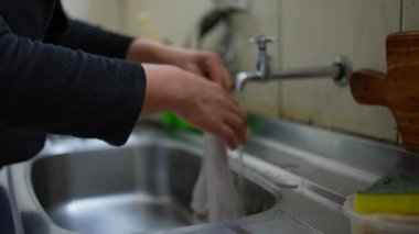 Güney Amerikalı bir kadının elleri bulaşık bezlerini mutfak lavabosuyla yıkıyor günlük ev içi aktivitelerle meşgul, suya bastırıyor.