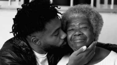 Genç Afrikalı Amerikalı torunun yaşlı büyükannesine şefkatle sarılıp öpmesi aile bağını simgeliyor siyah beyaz, yoğun tek renkli.