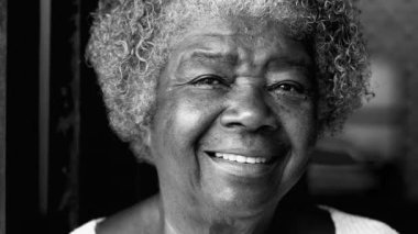 Gülümseyen Güney Amerikalı Afrika kökenli yaşlı bayan kameraya mutlu bir ifadeyle bakıyor, siyah ve beyaz. 80 'li yaşlarda siyahi bir kadının portresi, tek renkli.