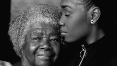 Siyah bir gencin nesiller arası portresi, aile bireyleri arasında sevgi dolu anlarda yaşlı bir büyükanneyi alnından öpen siyah ve beyaz monokromla bağlanan.