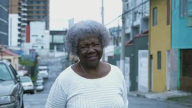 Güney Amerika kentsel ortamında duran gri saçlı yaşlı bilge bir kadının mutlu portresi. Afrikalı Amerikalı son sınıf öğrencisi kameraya gülümsüyor.