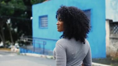 Genç, çekici, siyah Latin bir kadın sokakta yürürken kameraya doğru dönüyor. Kıvırcık saçlı, 20 'li yaşlarında, Güney Amerikalı yetişkin bir kız.