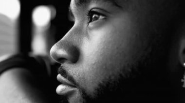 Derin düşüncelere dalmış genç siyahi bir adamın yakın plan yüzü. Yoğun monokromatik, siyah ve beyaz dönemlerde hayatı yansıtan 20 'li yaşlarda