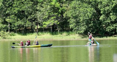 Çocuklar göl kenarında kanonun içinde kano yapıyor.