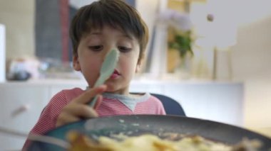 Yemek saatinde yemek yiyen küçük çocuk, 5 yaşındaki çocuğun yakın çekimi kaşıkla ezilmiş patatesler yiyen, yuvarlanan gözler ve akşam yemeği saatinde aptalca davranan çocuk.