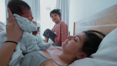 Anne, yeni doğmuş bebeğini kucağına alıp sabah yatarken 5 yaşındaki erkek kardeşi otantik yaşam tarzı aile sahnesinin yanında oturuyor.