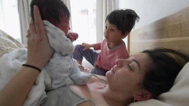 Otantik aile hayatı sahnesi, anne kucağında yeni doğmuş bir bebeği, erkek kardeşiyle birlikte yatakta yatarken, sabahları ailenin yeni bir üyesini gözlemliyor.