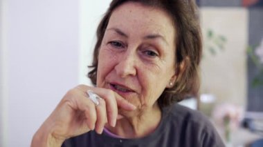 Üst düzey kadın, kamera önünde konuşulmayan birini dinliyor. Çenesinde el olan yaşlı bayan dikkatle dinliyor.