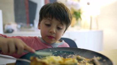 Küçük çocuk çatalla patates eziyor, çocuk yemek saatinde tabakta yemek yiyor, yemek yiyen çocuğun yakın plan yüzü.