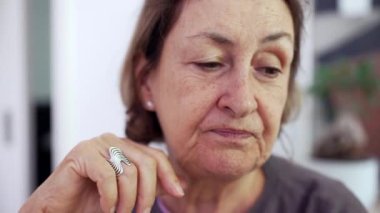 Eli çenesinde olan yaşlı bir kadının yakın plan portresi. Kameranın dışında birini dinleyip konuşuyordu.