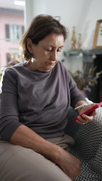 Старшая Женщина Смотрит Экран Телефона Сидя Дома Диване Серьезным Выражением — стоковое видео