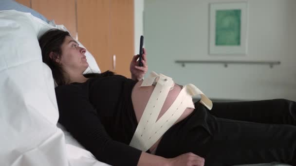 Kobieta Ciąży Sprawdzanie Telefonu Podczas Położenia Szpitalu Paskami Ultradźwiękowymi Pomiaru — Wideo stockowe