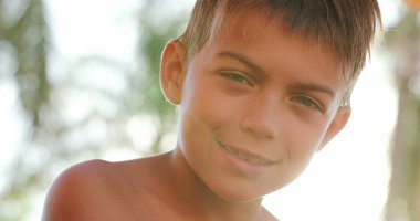 Child looking to camera smiling portrait of young boy outside with lens-flare sunlight