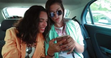Friend reaction putting hand in mouth looking at smartphone screen while riding taxi in backseat of car