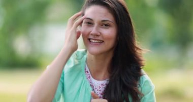 Casual millennial young woman adjusting hair rubbing face with hand outdoors at park