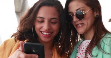 Cep telefonuna bakan iki kız, ekranı paylaşan kadınlar.